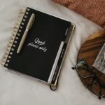 High-angle view of a notebook with 'Good plans only' sign, glasses, and coffee on a cozy setup.